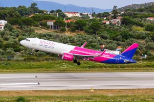 A Wizz Air plane taking off, surround by tress in the distance.